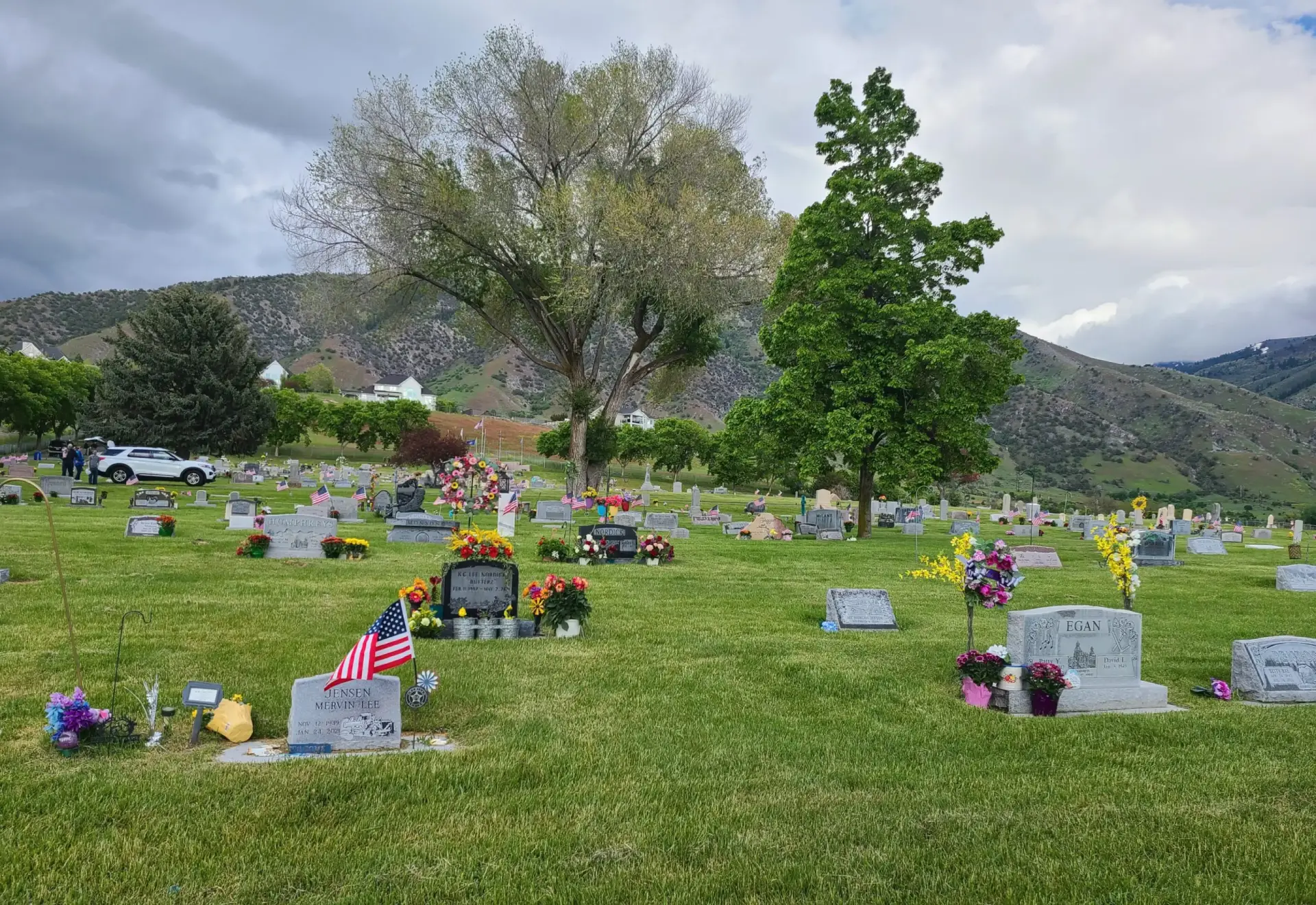 Cemetery with headstones and flowers under cloudy sky.